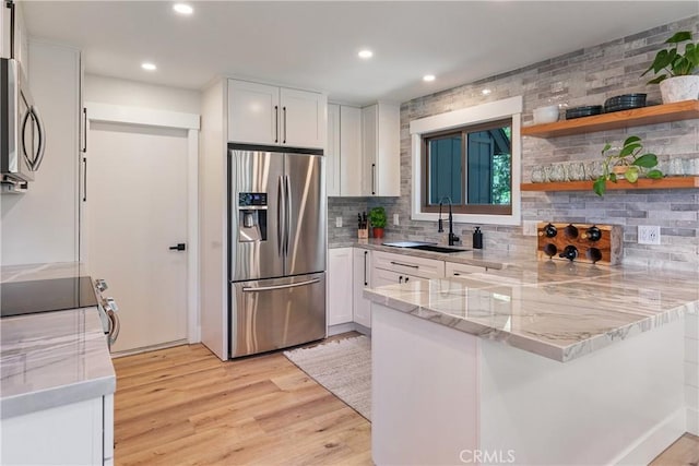 kitchen featuring kitchen peninsula, decorative backsplash, stainless steel appliances, sink, and white cabinetry