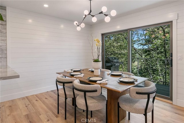 dining space featuring wood walls, light hardwood / wood-style flooring, and an inviting chandelier