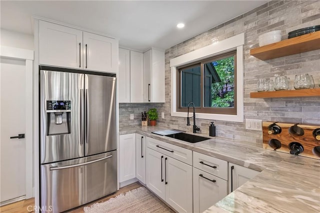 kitchen featuring backsplash, sink, stainless steel fridge, light stone countertops, and white cabinetry