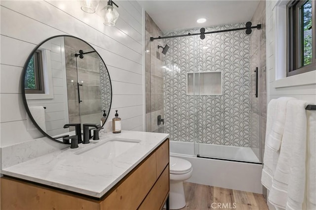 full bathroom featuring bath / shower combo with glass door, vanity, wood-type flooring, and toilet