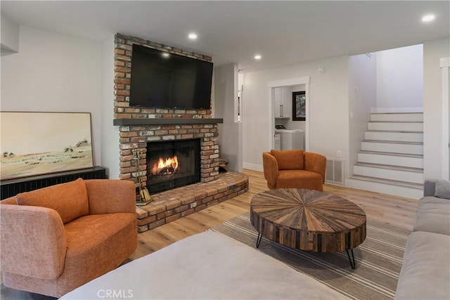 living room featuring wood-type flooring, a brick fireplace, and washer and clothes dryer