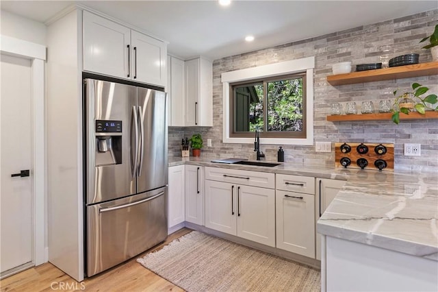 kitchen with light stone countertops, stainless steel fridge, white cabinetry, and sink