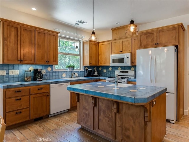 kitchen featuring white appliances, sink, decorative light fixtures, a breakfast bar area, and an island with sink