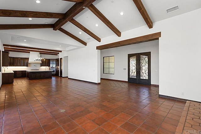 unfurnished living room featuring beam ceiling, french doors, dark tile patterned floors, and an inviting chandelier