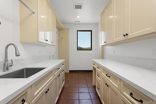 kitchen with light stone countertops, sink, dark tile patterned floors, and cream cabinetry