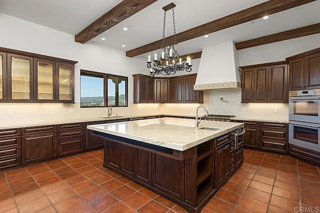 kitchen featuring beamed ceiling, a center island with sink, premium range hood, and sink