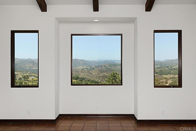 empty room with a mountain view, beam ceiling, and plenty of natural light