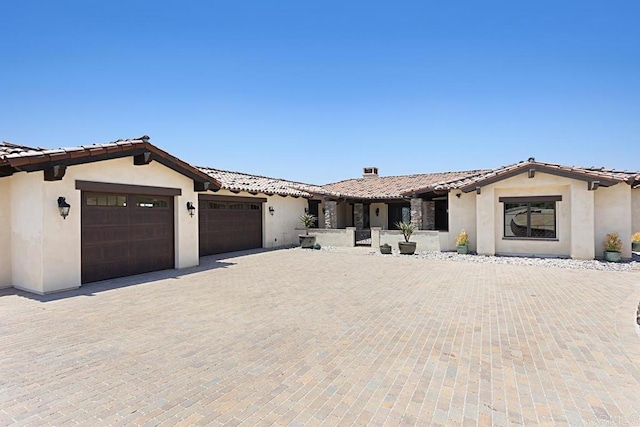 ranch-style house featuring a garage, stucco siding, a tiled roof, and decorative driveway