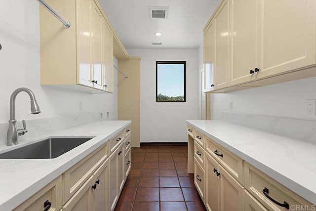 kitchen featuring light stone countertops, a sink, visible vents, and cream cabinetry