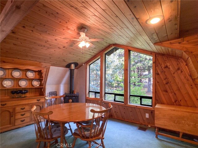 carpeted dining area with wood walls, a wood stove, lofted ceiling, and wood ceiling