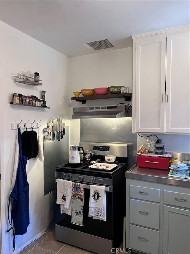 kitchen featuring stainless steel range oven, stainless steel counters, light tile patterned flooring, and white cabinets