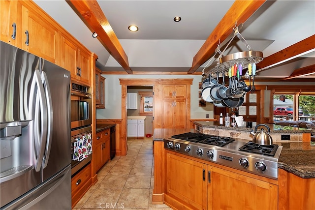 kitchen featuring beamed ceiling, appliances with stainless steel finishes, dark stone countertops, and light tile floors