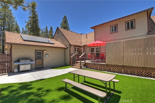 rear view of house with a wooden deck, a yard, and solar panels