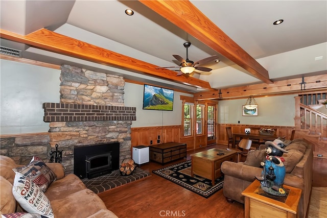 living room featuring beamed ceiling, a wood stove, hardwood / wood-style flooring, and ceiling fan