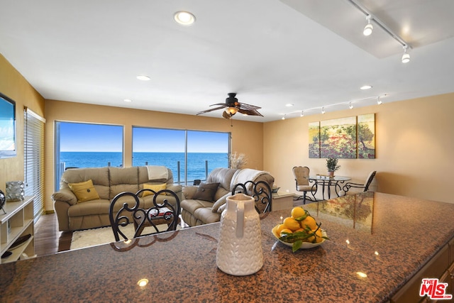 living room with rail lighting, a water view, hardwood / wood-style floors, and ceiling fan