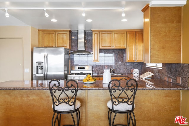 kitchen featuring tasteful backsplash, dark stone counters, range, stainless steel fridge with ice dispenser, and wall chimney range hood