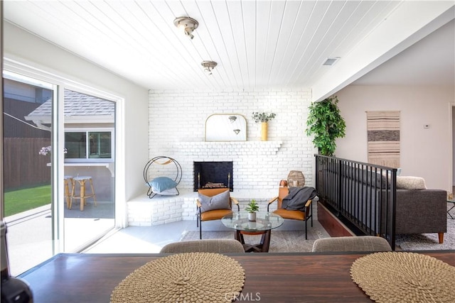 living room featuring beamed ceiling, brick wall, and a brick fireplace