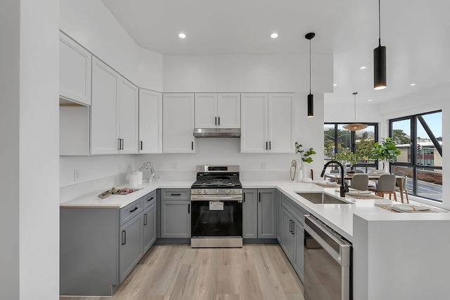 kitchen with gray cabinets, appliances with stainless steel finishes, light wood-type flooring, pendant lighting, and sink