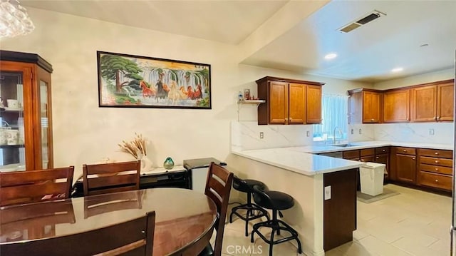 kitchen featuring kitchen peninsula, a kitchen bar, tasteful backsplash, sink, and pendant lighting