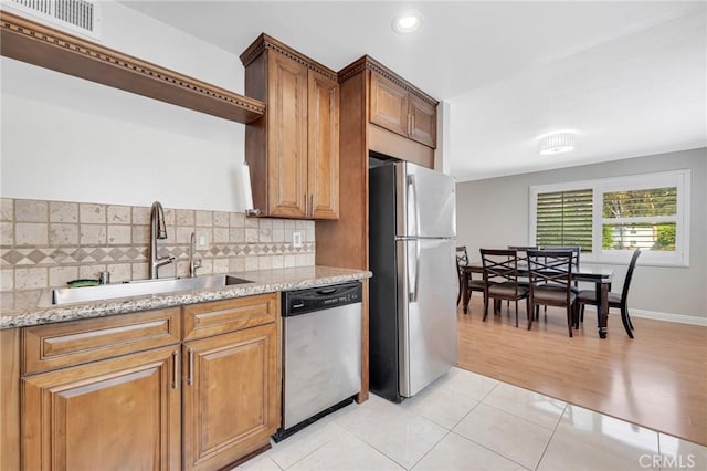 kitchen featuring light wood-type flooring, tasteful backsplash, light stone counters, stainless steel appliances, and sink