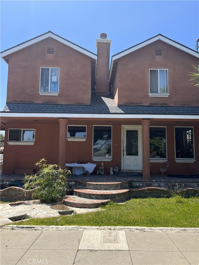 view of front of home with roof with shingles, a chimney, and stucco siding