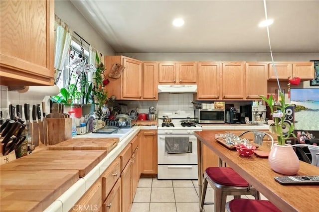 kitchen with decorative backsplash, light tile patterned floors, white range with gas cooktop, and light brown cabinetry