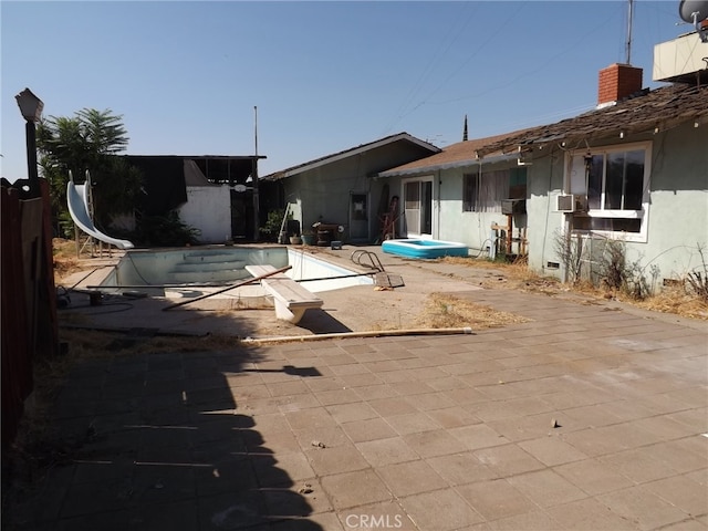 view of pool featuring cooling unit, a water slide, and a patio area