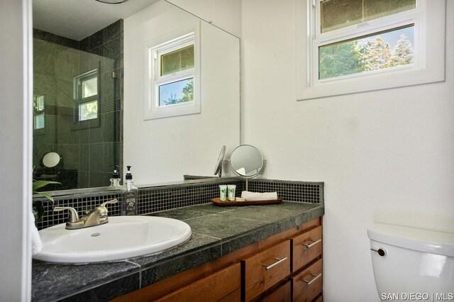 bathroom with toilet, tiled shower, tasteful backsplash, and vanity