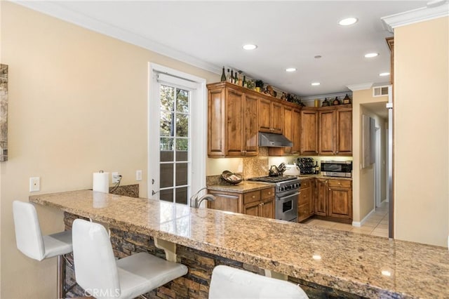 kitchen featuring light stone countertops, appliances with stainless steel finishes, light tile patterned flooring, kitchen peninsula, and a breakfast bar area