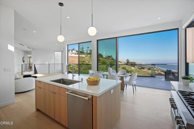 kitchen with pendant lighting, a center island with sink, a water view, sink, and light wood-type flooring