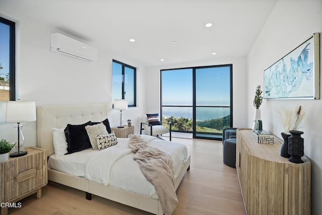 bedroom with a wall of windows, light hardwood / wood-style flooring, and a wall mounted AC