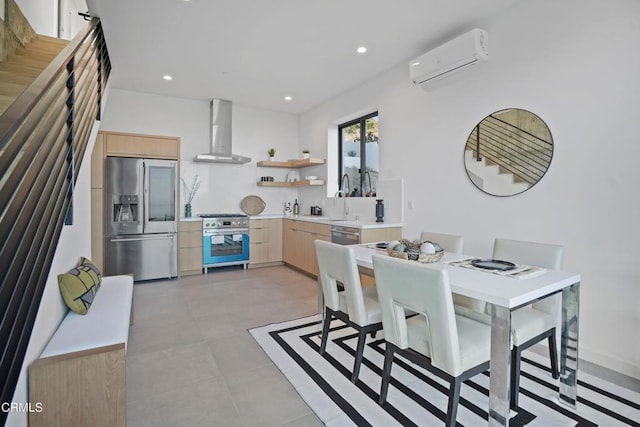 kitchen with appliances with stainless steel finishes, light brown cabinetry, wall chimney exhaust hood, a wall mounted AC, and sink