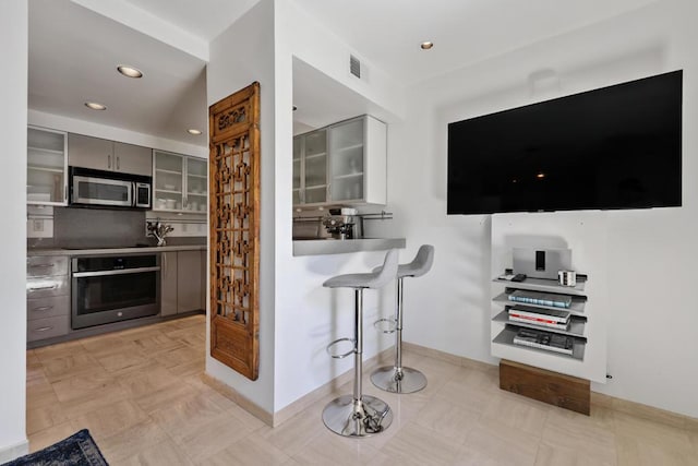 kitchen with stainless steel counters, gray cabinets, a kitchen breakfast bar, and appliances with stainless steel finishes