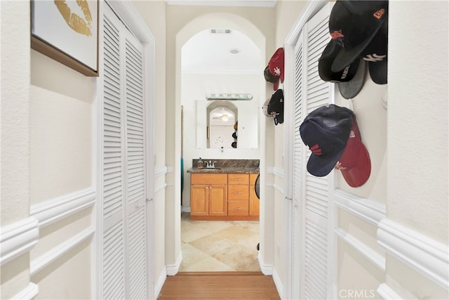 hallway with sink, light wood-type flooring, and crown molding