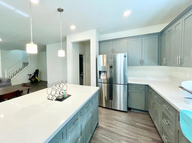 kitchen with light stone countertops, hanging light fixtures, stainless steel refrigerator with ice dispenser, gray cabinets, and light wood-type flooring