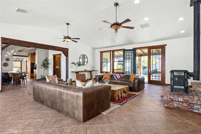 tiled living room with a wood stove, a healthy amount of sunlight, ceiling fan, and vaulted ceiling