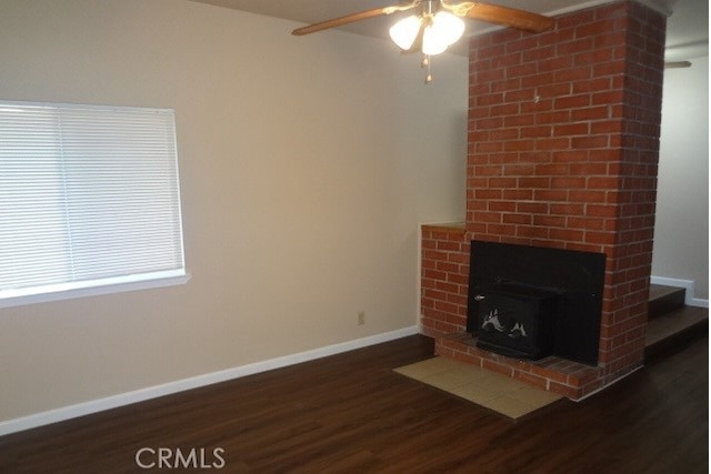 unfurnished living room with a brick fireplace, ceiling fan, and dark wood-type flooring