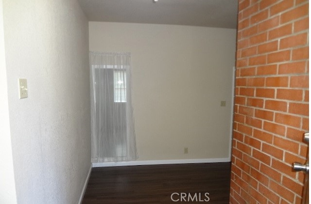 spare room with brick wall and dark wood-type flooring