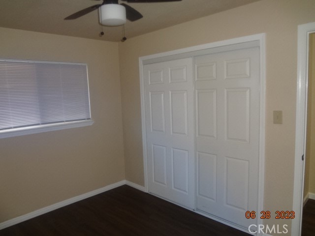 unfurnished bedroom with ceiling fan, a closet, and dark wood-type flooring