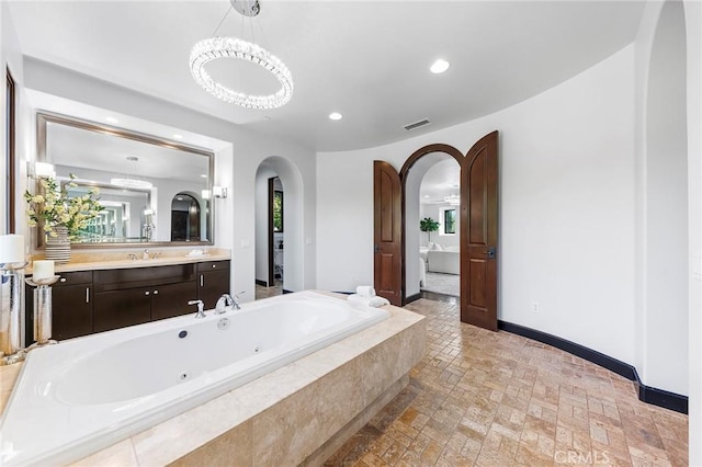 bathroom with vanity, tiled tub, and a chandelier