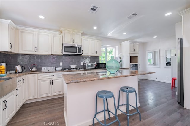 kitchen with dark hardwood / wood-style floors, light stone countertops, appliances with stainless steel finishes, a kitchen island, and a kitchen bar