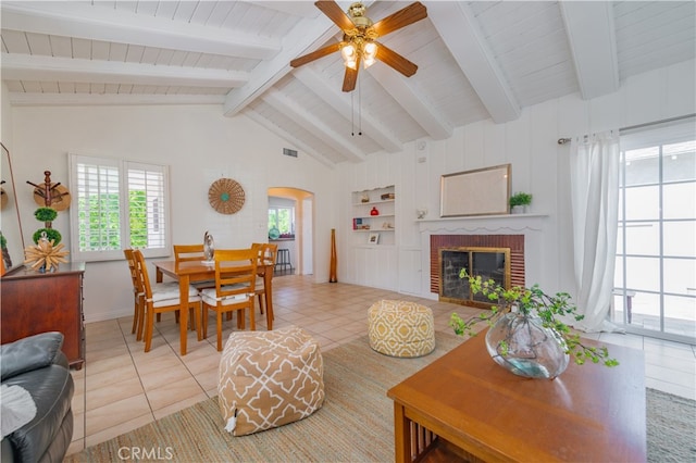 living room with a brick fireplace, tile patterned floors, ceiling fan, beam ceiling, and built in features