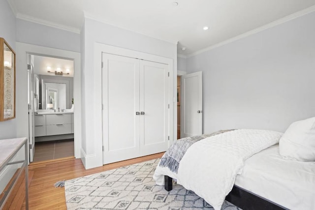 bedroom with connected bathroom, light hardwood / wood-style flooring, ornamental molding, and a closet