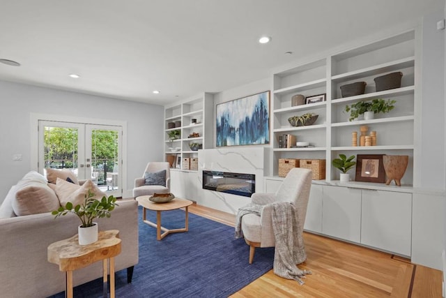 living room with light hardwood / wood-style flooring, built in features, a high end fireplace, and french doors