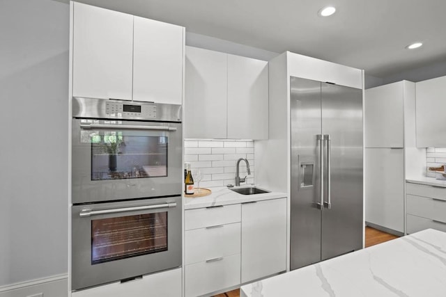 kitchen featuring sink, stainless steel appliances, light stone countertops, white cabinets, and decorative backsplash