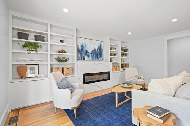 living room with built in shelves, wood-type flooring, and a premium fireplace