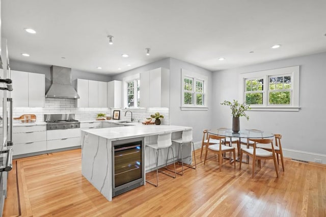 kitchen with wine cooler, sink, wall chimney range hood, and white cabinets