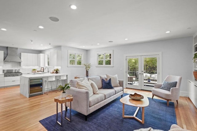 living room with sink, light hardwood / wood-style flooring, beverage cooler, and french doors