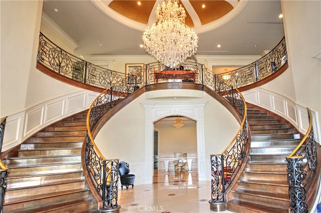 stairs featuring a notable chandelier, a high ceiling, ornate columns, and crown molding