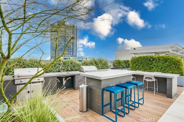 view of patio / terrace with area for grilling, a wooden deck, exterior bar, and an outdoor kitchen